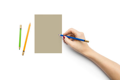 Close-up of hand holding pencils against white background