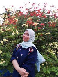 Portrait of a smiling young woman standing against plants