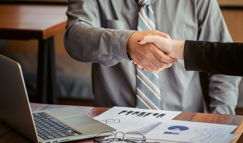 Midsection of businessman and colleague shaking hands over table at office