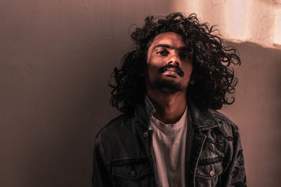 Portrait of young man looking away against wall