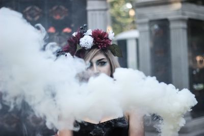 Portrait of woman wearing flowers while standing with smoke