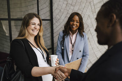 Smiling pregnant businesswoman greeting male colleague while doing handshake during seminar at convention center