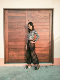 Full length portrait of young woman standing against door