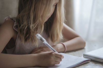 Midsection of girl writing on notebook at home