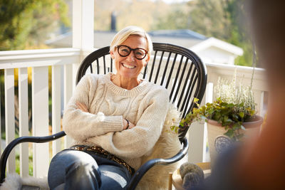 Portrait of cheerful mature woman with arms crossed sitting on porch