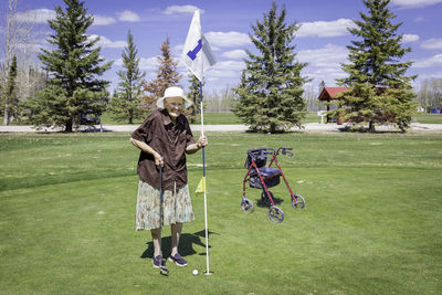 Senior woman standing on golf course against sky