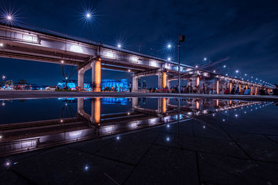 Illuminated bridge over river against sky in city at night