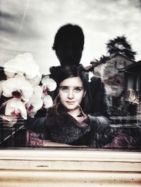 Portrait of young woman with flowers against sky