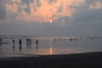 Silhouette people standing on beach against sky during sunset