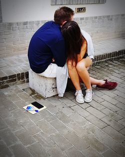 Rear view of couple kissing on footpath in city