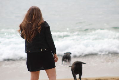 Rear view of woman with dog standing at beach