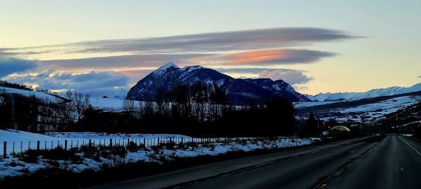 Road by snow covered mountains against sky during sunset