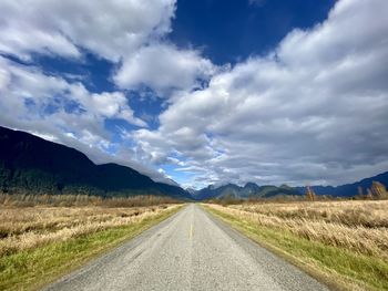 Empty road amidst field against sky