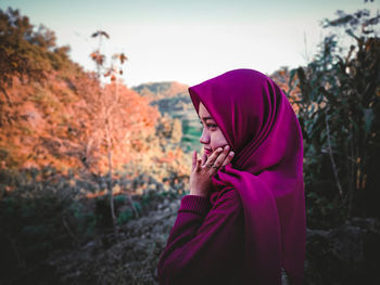 Side view of woman holding pink umbrella against trees