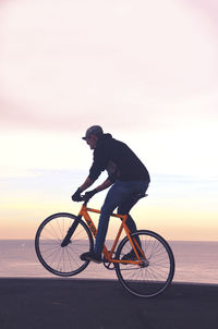 Side view of man riding bicycle by sea against sky