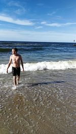 Full length of shirtless man walking at beach against sky
