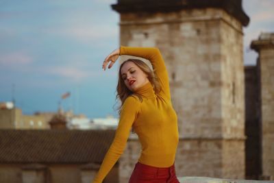 Beautiful young woman standing against sky in city