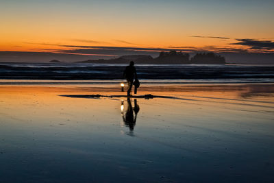 Silhouette man with oil lamp walking at beach against sky during sunset
