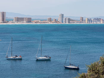 Sailboats in sea by buildings against clear sky
