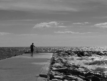Rear view of man walking on pier by sea against sky