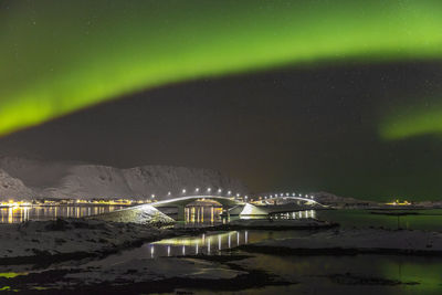 Illuminated city by sea against sky at night