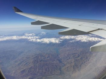 Aerial view of aircraft wing over landscape against blue sky