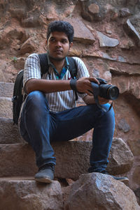 Full length of young man sitting on rock against wall