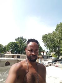 Portrait of shirtless man standing in swimming pool against sky