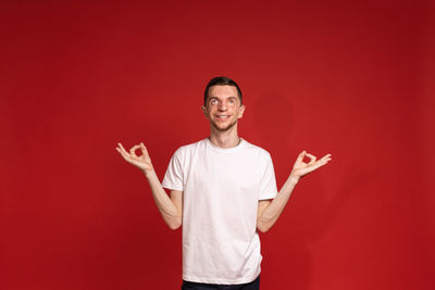 Portrait of young woman with arms raised standing against yellow background