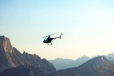 Low angle view of helicopter flying over mountains against clear sky