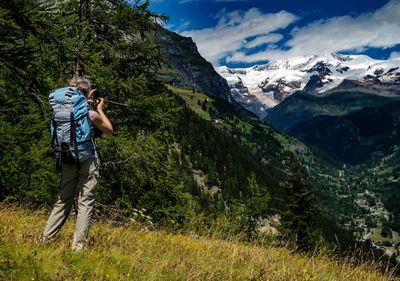 Woman photographing while standing on grass against mountains and sky