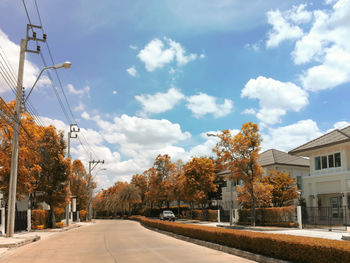 Road amidst trees and buildings against sky