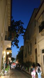 People on sidewalk amidst buildings in city at night