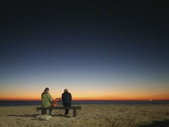 Rear view of women sitting on beach against sky during sunset