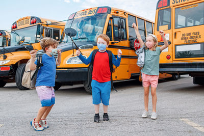 Happy excited children kids students in protective face masks jumping near school yellow bus 