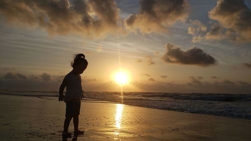 Silhouette woman standing on beach against sky during sunset