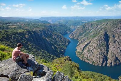 Rear view of woman sitting on rock by sea against sky