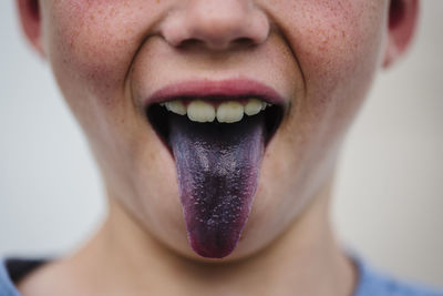 Midsection of boy sticking out purple tongue