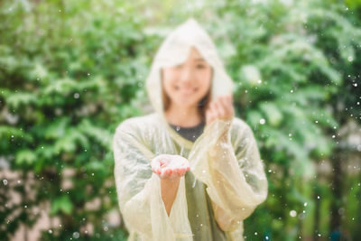 Smiling woman in raincoat standing against trees during rainy season