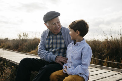 Happy grandfather sitting with his grandson on boardwalk looking at each other