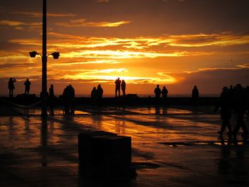 Silhouette people standing on beach against sky during sunset