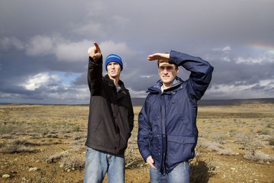 Friends looking away while standing on field against cloudy sky