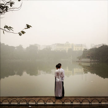 REAR VIEW OF MAN STANDING ON LAKE
