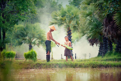 Side view of shirtless mature farmer with grandson working on farm by lake