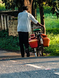 Rear view of man walking with bicycle on road