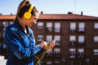 Side view of man using mobile phone against building