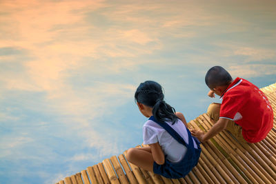 High angle view of siblings sitting on pier over lake during sunset