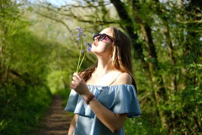 Teenage girl smelling flowers while standing against trees at forest