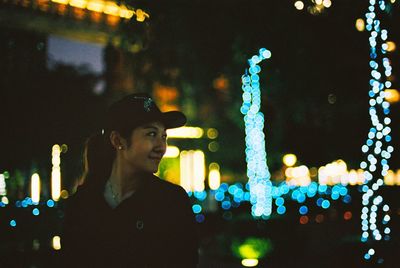 Smiling mid adult woman wearing cap while looking away in city at night