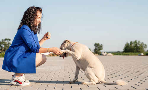 Side view of woman with dog on footpath against clear sky